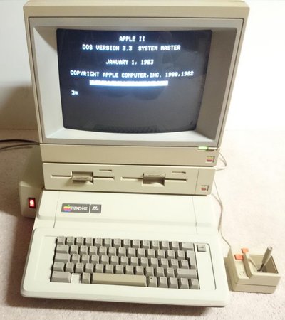 Apple IIe allumé, écran affichant l'invite DOS 3.3 Apple, avec double lecteur de disquettes et manette
