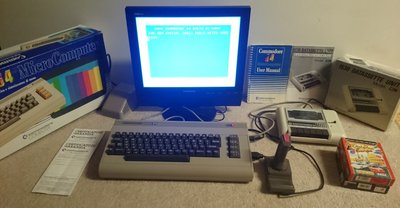 Commodore 64 avec écran affichant l'invite BASIC, boîte d'origine, manuels, lecteur de cassette Datassette et manette