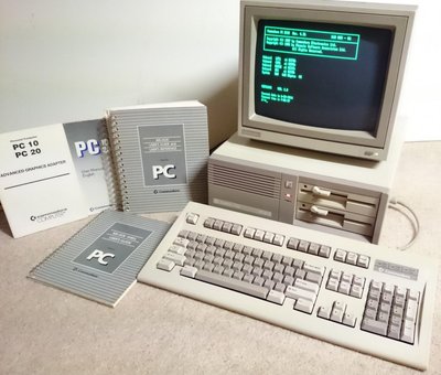 Commodore PC-10 III : unité centrale, écran affichant l'invite MS-DOS et clavier 102 touches, avec les manuels d'origine