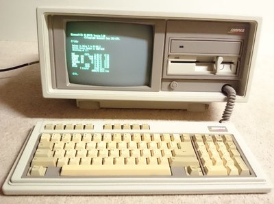 Compaq Portable II ouvert, écran monochrome affichant MS-DOS, clavier détaché posé devant l'unité centrale