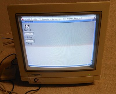 Moniteur Commodore relié à un Amiga 2000, affichant le bureau Workbench avec les icônes Ram Disk, System et Work