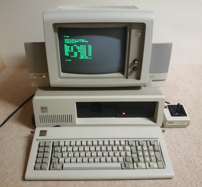 IBM 5150 avec écran monochrome affichant l'invite MS-DOS, clavier IBM et haut-parleurs d'origine
