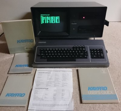Kaypro 4 ouvert avec écran vert affichant CP/M, clavier détachable et manuels d'origine Kaypro posés autour