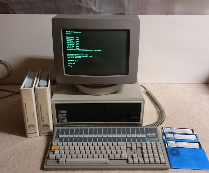 Olivetti M24 sous MS-DOS, écran affichant un diagnostic système, clavier et manuels Olivetti posés devant l'unité centrale