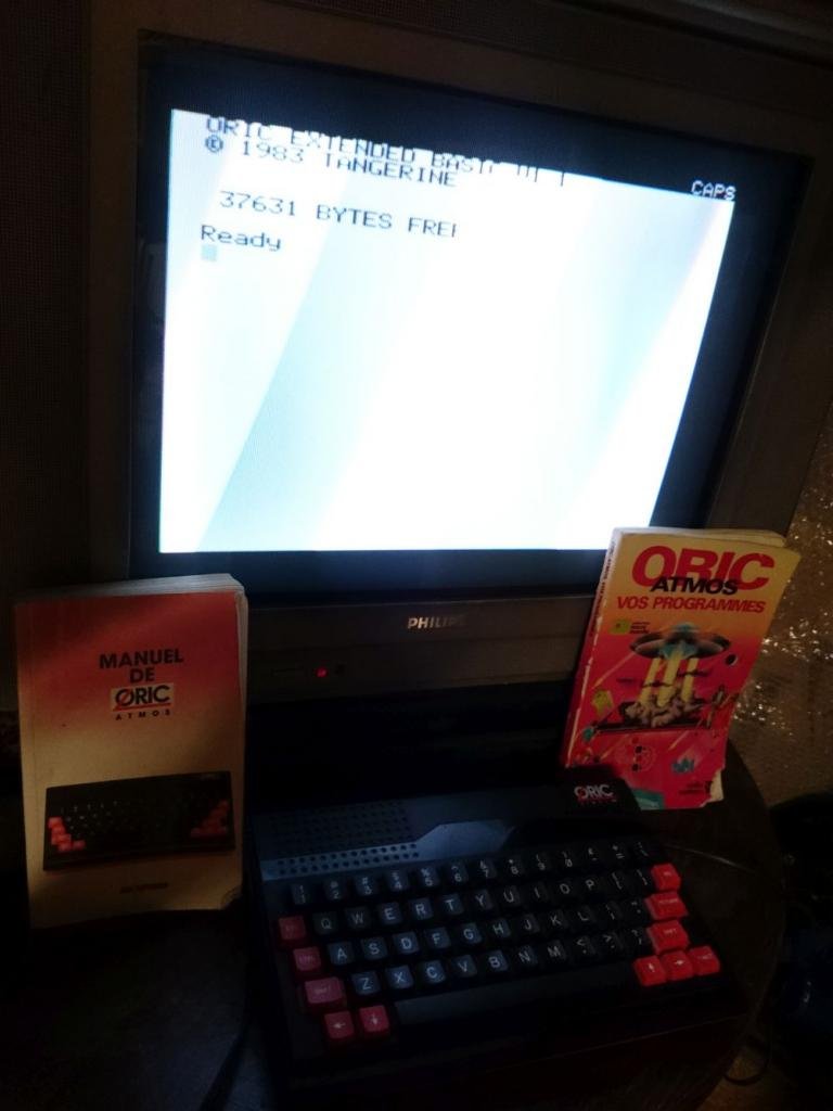 Oric Atmos avec écran affichant l'invite Extended Basic 1.1, manuel et boîte de programmes d'origine