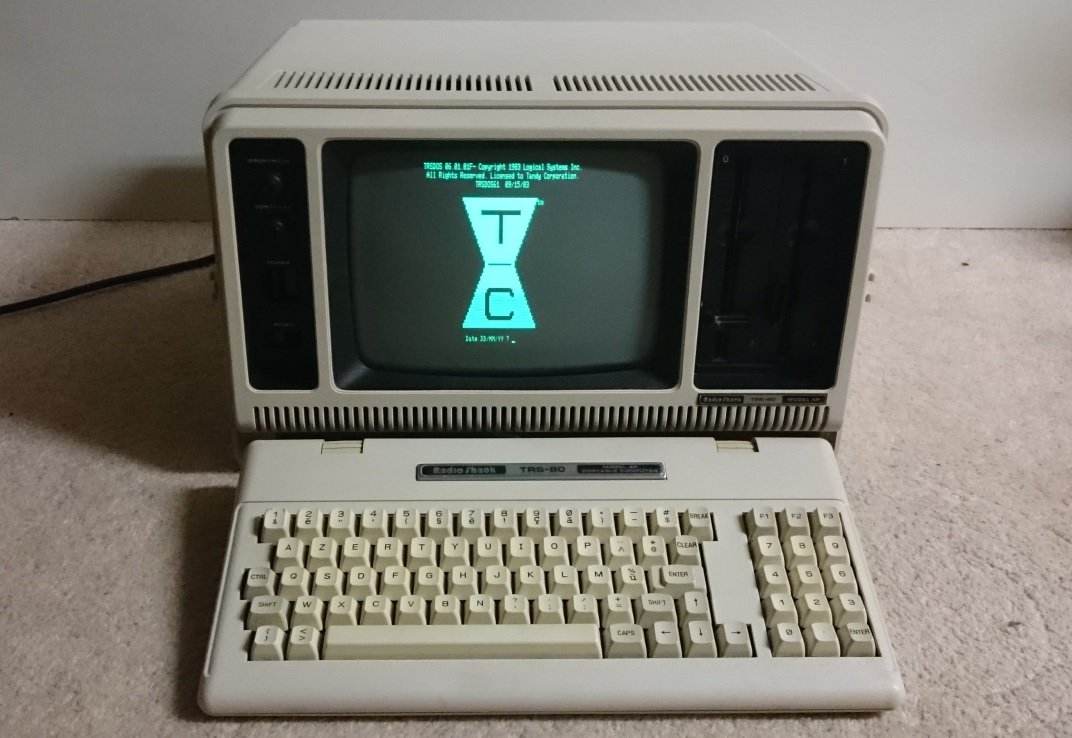 Tandy TRS-80 Model 4P ouvert, écran affichant TRSDOS au démarrage, clavier machine à écrire posé devant l'unité centrale