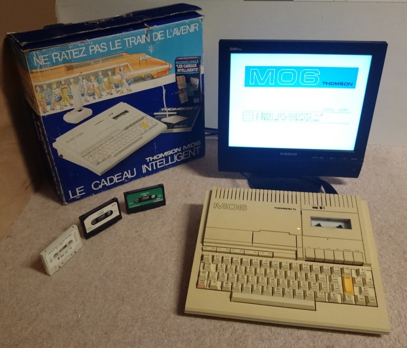 Thomson MO6 avec écran affichant le menu système, boîte d'origine et cassettes de logiciels