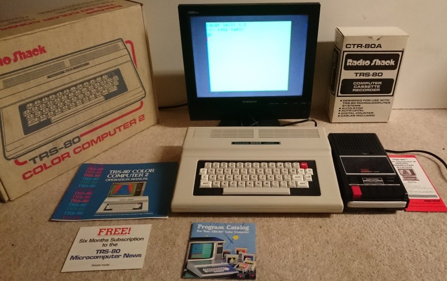 TRS-80 Color Computer 2 avec boîte d'origine, écran affichant l'invite BASIC couleur et lecteur de cassette Radio Shack